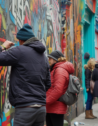 An artist paints a vibrant mural on a historic Dublin building, blending traditional Irish symbols with modern expressions, as intrigued passersby observe and capture the moment.