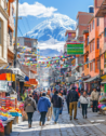Energetic scene of travelers exploring La Paz's colorful markets, with the majestic Illimani Mountain towering in the background, showcasing the vibrant street life and culture.