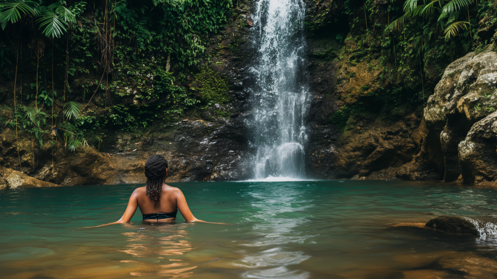 Woman swimming towards a tropical waterfall.