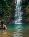 Woman swimming towards a tropical waterfall.