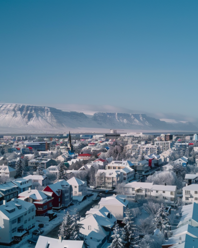 Aerial view of Reykjavik with colorful rooftops and snow-capped mountains in the background on a clear winter day.