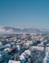 Aerial view of Reykjavik with colorful rooftops and snow-capped mountains in the background on a clear winter day.